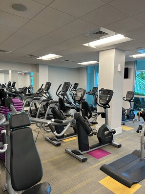 A gym with multiple cardio machines, a mirror, and a view of a staircase outside. - Cozy 1-bedroom apartment with AC in wonderful Fort Myers (Fort Myers)