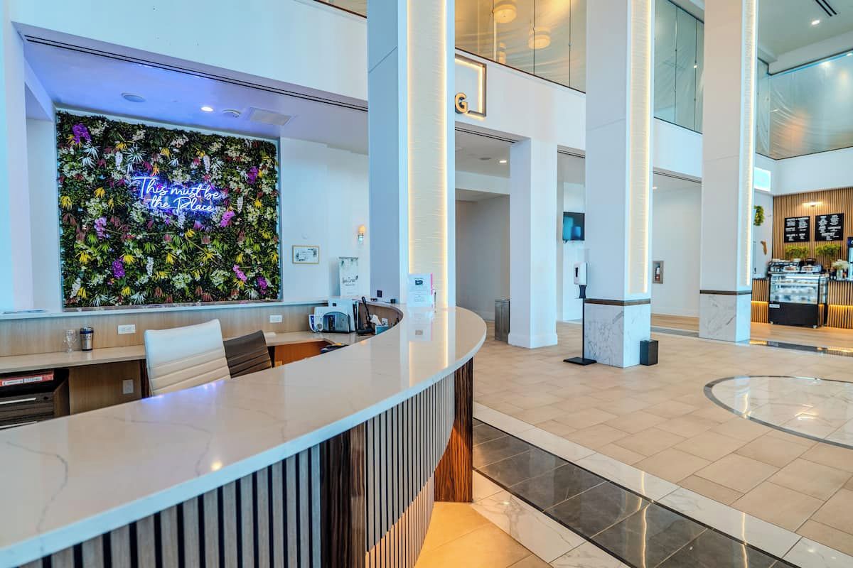 A hotel reception area with a curved reception desk, a floral wall, and a view of the lobby.