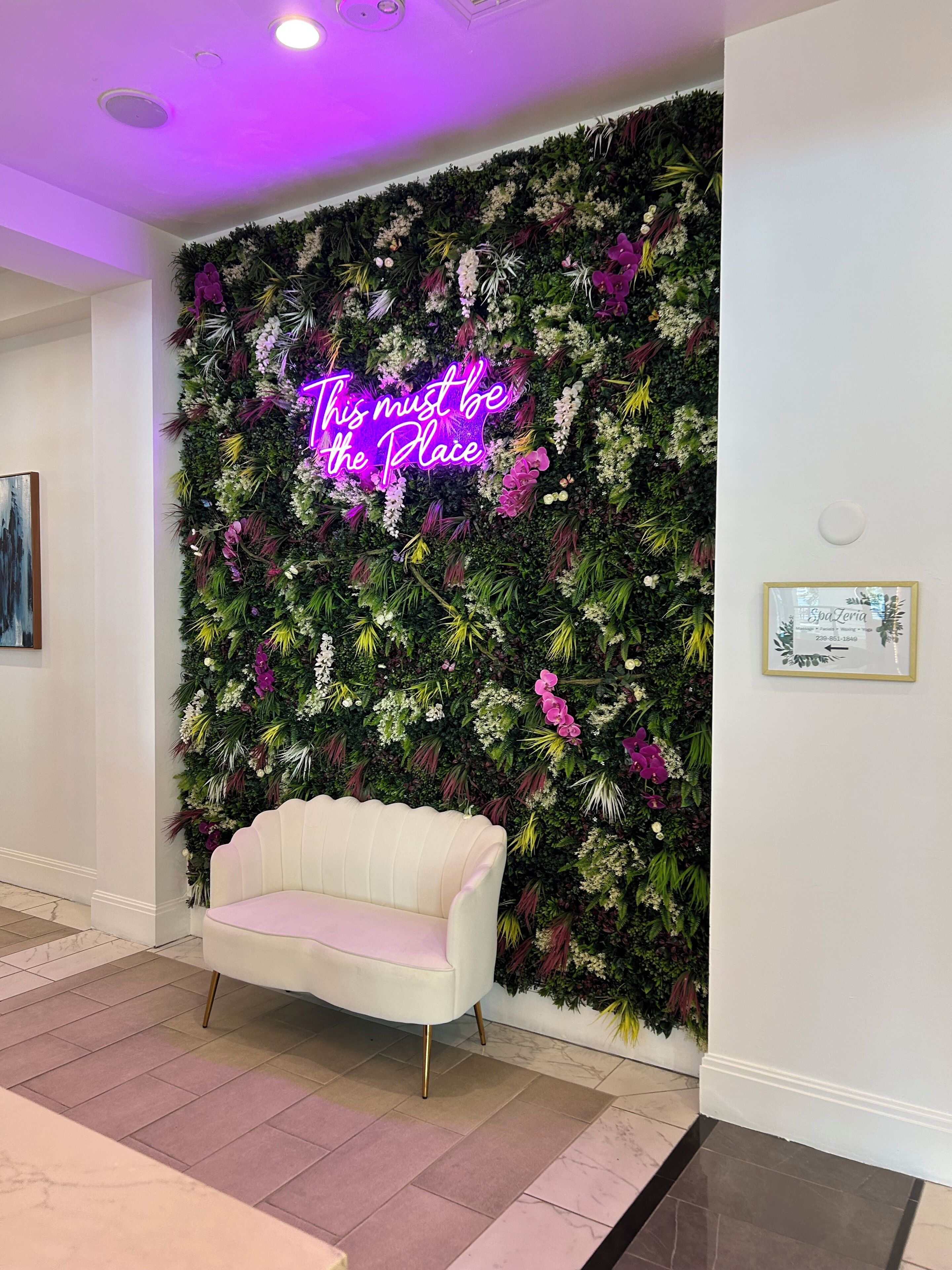 Ein Zimmer mit einem weißen Sofa, einer Wand mit Blumenmuster und einer Neonreklame.