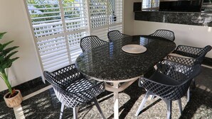 Een ronde eettafel met zes stoelen, een potplant en een raam met luxaflex.