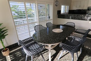 Una mesa redonda de comedor con seis sillas, una planta en maceta y una ventana con persianas.