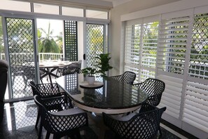 Een ronde glazen tafel met zes stoelen, een bloempot en zicht op palmbomen door een muggenhoring.