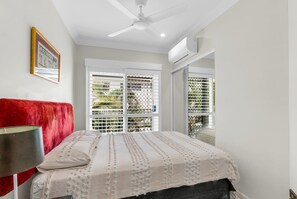 Een slaapkamer met een bed, een rood hoofdeinde, een plafondventilator en een raam met zonwering.