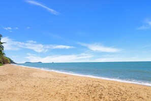 Una playa con cielos despejados, mar tranquilo y accidentes geográficos a lo lejos.
