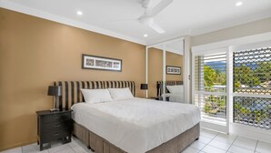 Een slaapkamer met een bed, nachtkastjes, een plafondventilator en een raam met uitzicht.