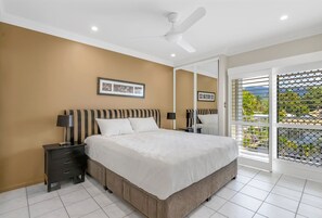 Un dormitorio con cama, mesitas de noche, ventilador de techo y ventana con vistas.