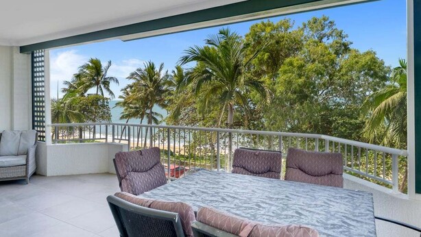 A balcony with a table and chairs, overlooking a tropical landscape with palm trees and a clear sky.