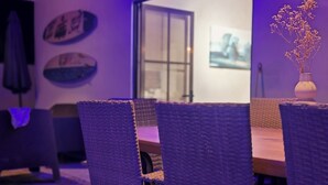 Une pièce comprenant une table à manger, des chaises en osier, un ventilateur de plafond et un panneau sur lequel on peut lire : « Ne vous inquiétez pas, soyez heureux. »
