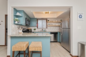 A modern kitchen with teal cabinetry, a stainless steel refrigerator, and a central island with stools. - Steps to Beach 3BR Coastal Retreat Sleeps 10 (North Myrtle Beach)