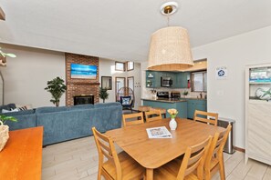 A modern living room with a blue sofa, a wooden dining table, and a kitchen area with teal cabinets. - Steps to Beach 3BR Coastal Retreat Sleeps 10 (North Myrtle Beach)