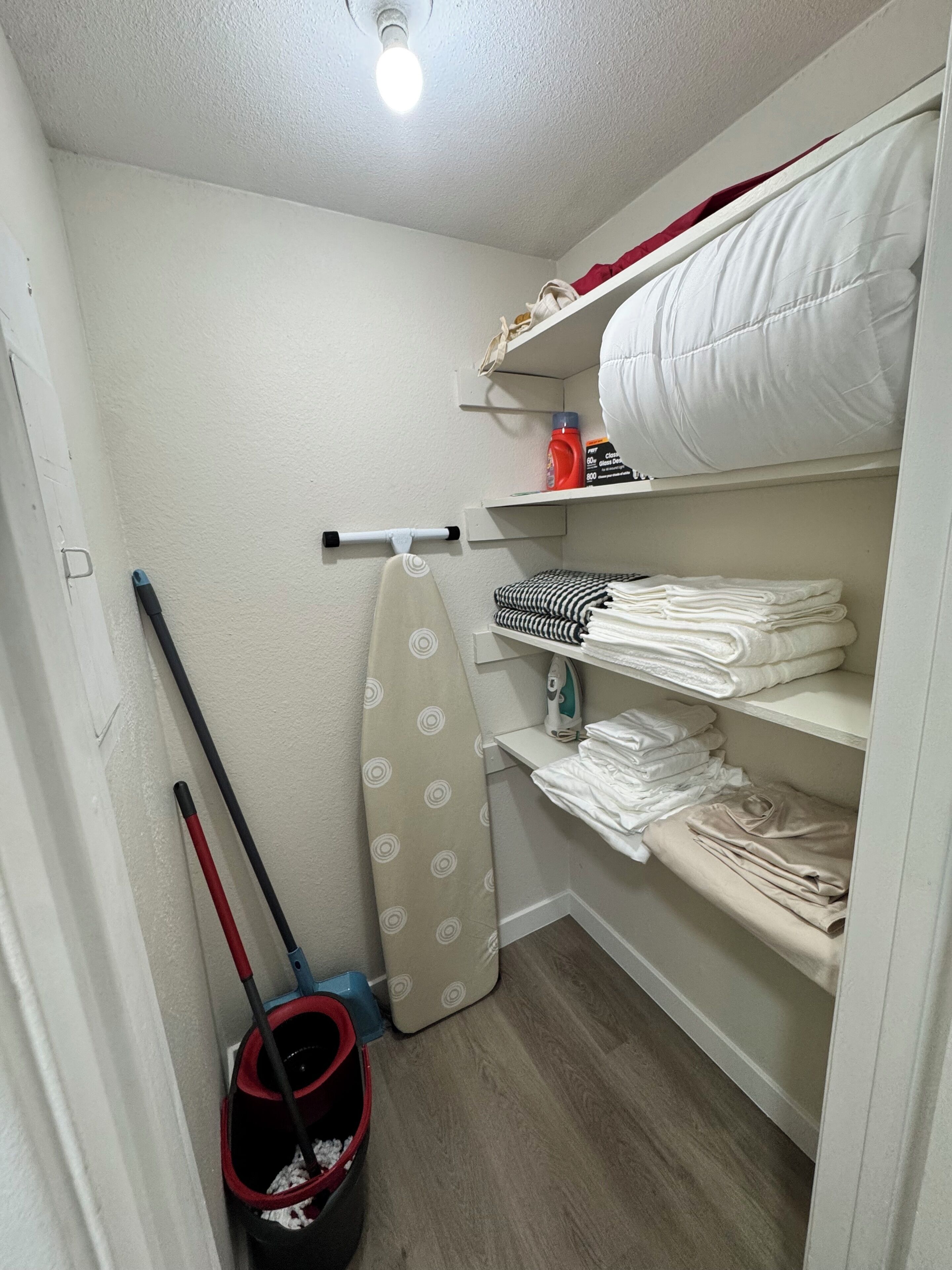 A laundry room with a drying rack, ironing board, and neatly stacked towels.