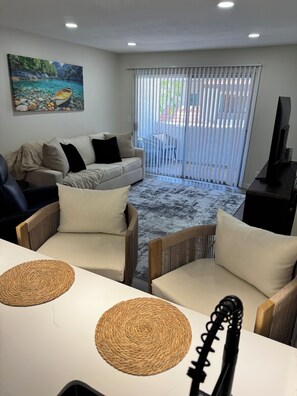 Ein Wohnzimmer mit einer Couch, Sesseln, einem Fernseher und einem Bild an der Wand.