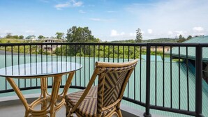 A balcony with a wicker chair and a glass table, overlooking a green landscape and buildings. - The Lakeside Stay (Nuwara Eliya)