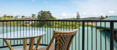 Un balcón con una silla de mimbre y una mesa de vidrio, con vistas a un paisaje verde y edificios.