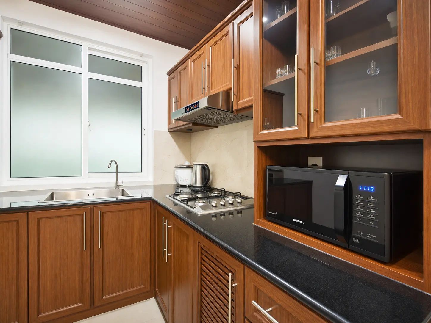 Une cuisine avec des meubles de rangement en bois, un évier en acier inoxydable, une cuisinière et un micro-ondes noir.