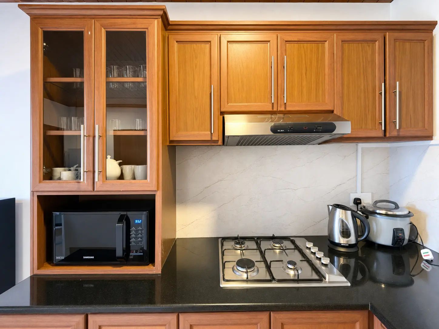 Une cuisine avec des meubles de rangement en bois, un four à micro-ondes encastré, une cuisinière à gaz et une bouilloire.