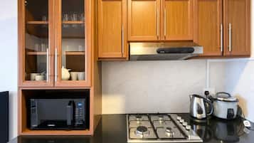 Une cuisine avec des meubles de rangement en bois, un four à micro-ondes encastré, une cuisinière à gaz et une bouilloire.