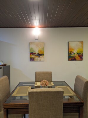 A conference room with a glass table, two chairs, a vase with flowers, and two abstract paintings on the wall.