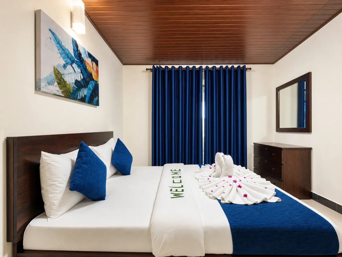 A hotel room with a bed, a headboard, a wall-mounted artwork, a window with curtains, a bedside table, and a mirror.