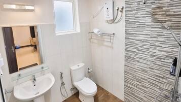 A bathroom with a toilet, two sinks, a shower, and a window.