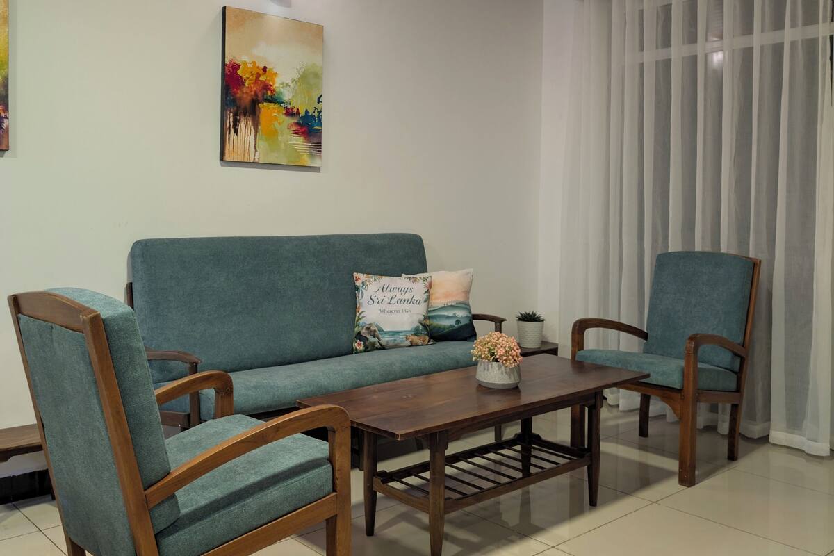 Un salon comprenant un canapé, deux fauteuils, une table basse, un tableau et une fenêtre avec des rideaux.