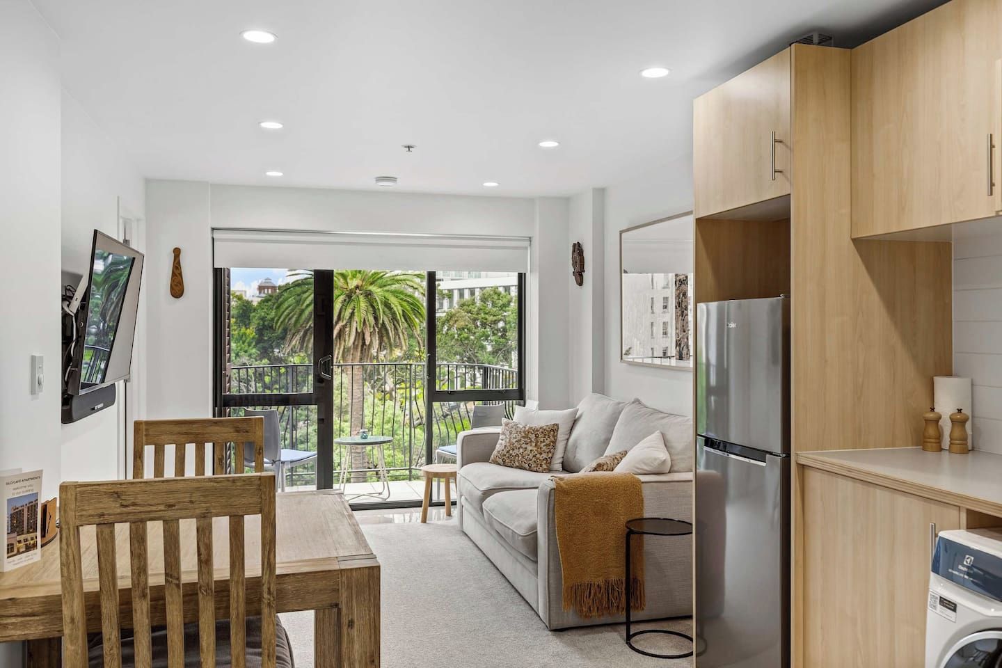 A modern apartment with a balcony, a dining area, a living room with a sofa, and a kitchen with a refrigerator.