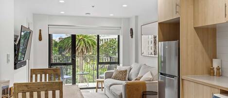 A modern apartment with a balcony, a dining area, a living room with a sofa, and a kitchen with a refrigerator.