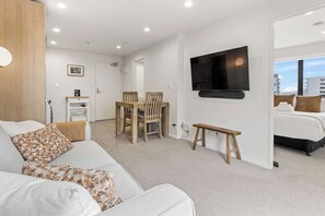 A modern hotel room with a white sofa, a dining table with chairs, a TV mounted on the wall, and a bed with a view of the city. - City Apt with Balcony and Parking by Zodiak Stays (Auckland)