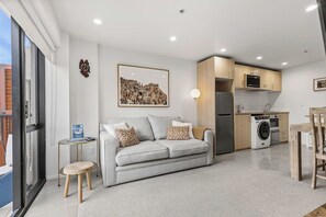 Ein modernes Apartment mit einem grauen Sofa, einem Esstisch, einer Küche mit Geräte und einem großen Fenster.