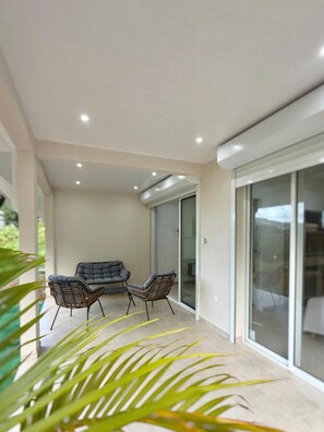 A modern patio with two chairs and a sofa, a glass door leading to a balcony, and a plant in the foreground. - The cos cocoon, less than 10 minutes from the airport. (Ducos)