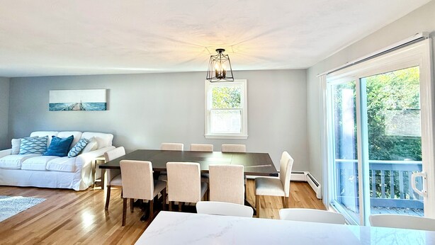 A modern living room with a dining area, a sofa, and a large window. - Coastal Bristol, RI 4-Bedroom Home Near Downtown, RWU, & Wedding Venues (Bristol)