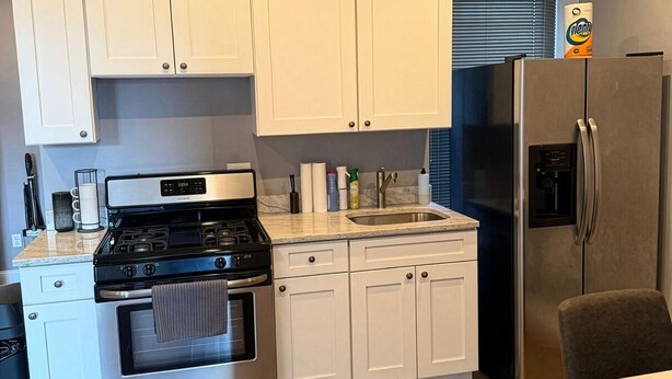 A kitchen with white cabinets, a stainless steel stove, a refrigerator, and a wooden floor. - 2-bedroom Apartment in Central Brooklyn (Brooklyn)
