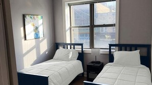A bedroom with two beds, a window, and a nightstand. - 2-bedroom Apartment in Central Brooklyn (Brooklyn)