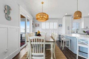A modern kitchen with white cabinetry, a central island, and a dining area with white chairs. - Long Call - 5-bedroom retreat in Oak Island, perfect for families and pets! (Oak Island)