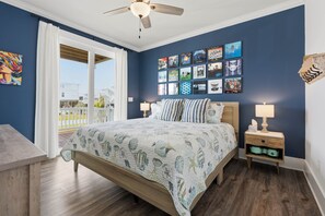 A bedroom with a bed, nightstands, a ceiling fan, and a balcony with a view. - Long Call - 5-bedroom retreat in Oak Island, perfect for families and pets! (Oak Island)