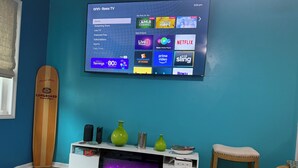 Ein Wohnzimmer mit einem an der Wand befestigten Flachbildfernseher, einem hölzernen Surfbrett, einer weißen Unterhaltungsanlage mit Kamin und einer roten gepolsterten Bank.