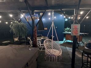 A cozy outdoor seating area with hanging chairs, a table, and string lights. - Sunny & SAndy Surf Social , 3/2 Mid Century Vibes ,Sunset Vibes, Coastal Stays (Myrtle Beach)