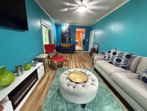 A living room with a sofa, armchair, ottoman, and a television. - Sunny & SAndy Surf Social , 3/2 Mid Century Vibes ,Sunset Vibes, Coastal Stays (Myrtle Beach)