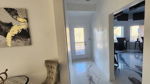 A hallway with a door leading to a balcony, a marble floor, and a piece of abstract art on the wall.