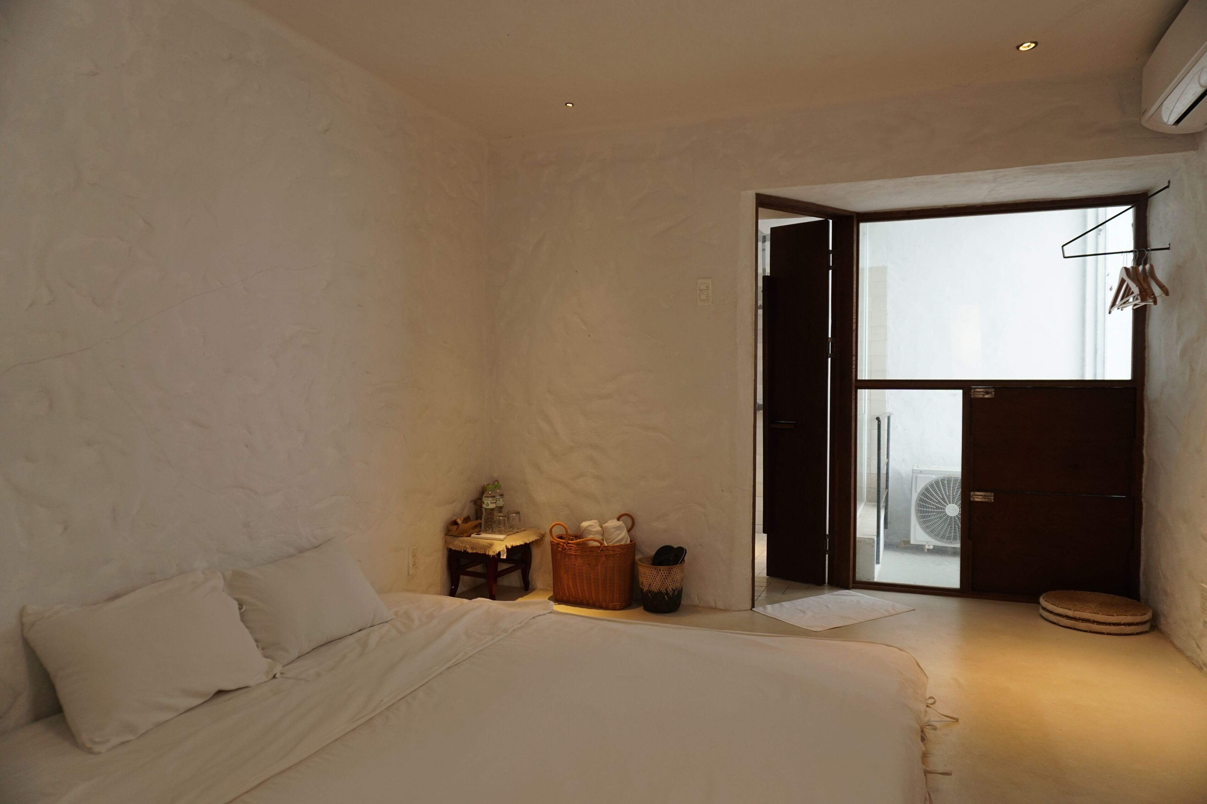 A bedroom with a bed, a small table with a lamp, a basket, and a door leading to a balcony.