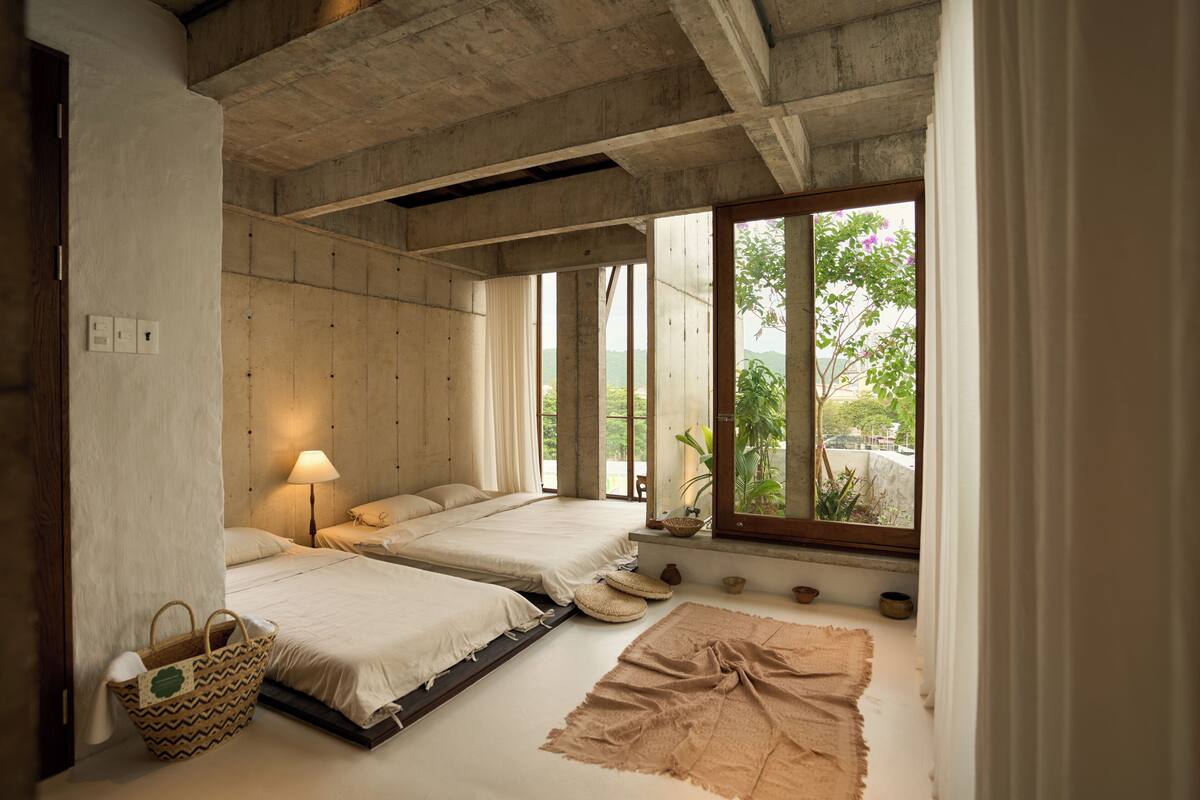 A room with two beds, a window with a view, a lamp, and a woven basket.