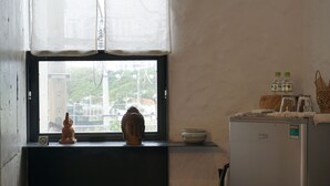 A window with a view of a building, a Buddha statue, a refrigerator, and a shelf with bottles and a bowl. - The Still (Nam Nha Trang)
