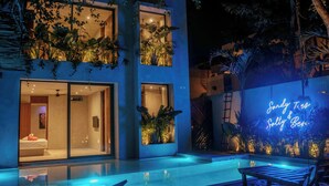 A modern building with a swimming pool, glass doors, and a neon sign.