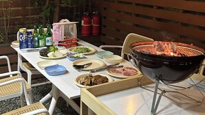 Un espace extérieur aménagé pour les repas, avec un barbecue, des tables, des chaises et divers aliments.