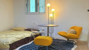 Une chambre à coucher avec un lit, une chaise, une petite table et une lampe sur pied.