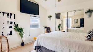 Une chambre à coucher avec un lit, un ventilateur de plafond, un grand miroir, une télévision et une fenêtre.