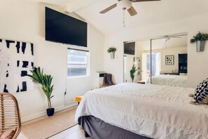 Ein Schlafzimmer mit Bett, Deckenventilator, großem Spiegel, Fernseher und Fenster.