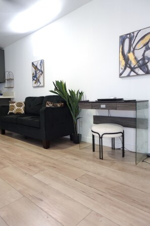 Een moderne woonkamer met een zwarte bank, een glazen bureau en een potplant.