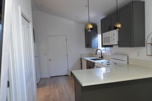 Een moderne keuken met een wit aanrecht, donkere kastjes, een magnetron en hangende lampen.