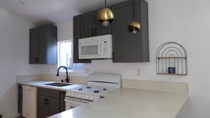 Une cuisine avec des meubles de couleur sombre, un micro-ondes blanc, une cuisinière et des luminaires suspendus.